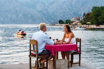 Fototapeten Couple in love drinking wine on romantic dinner at sunset on the beach. © NDABCREATIVITY