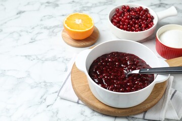 Fresh cranberry sauce in bowl served on white marble table, space for text