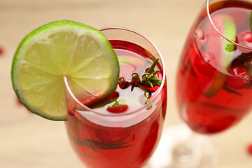 Tasty cranberry cocktail with rosemary and lime in glasses on beige table, closeup