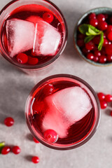 Tasty cranberry juice with ice cubes in glasses and fresh berries on light grey table, flat lay