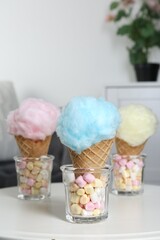 Sweet cotton candies in waffle cones and marshmallows on white table indoors, closeup