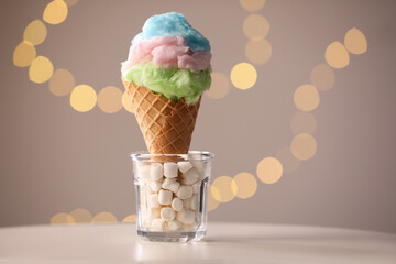 Sweet cotton candy in waffle cone on table against blurred lights, closeup