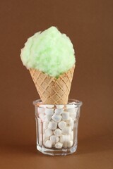 Sweet cotton candy in waffle cone on brown background, closeup