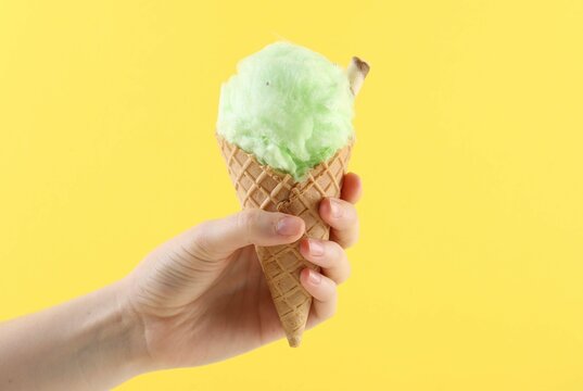 Woman holding waffle cone with cotton candy on yellow background, closeup
