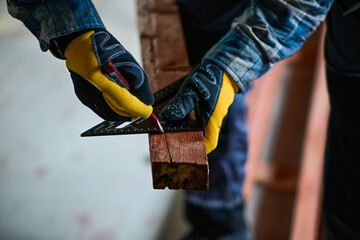 a worker in yellow gloves marks a straight line with a right-angled triangle and a wood pencil to...