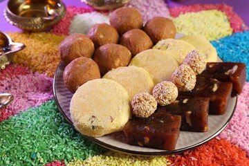 Fototapeta na wymiar Diwali celebration. Tasty Indian sweets, colorful rangoli and diya lamps on table, closeup