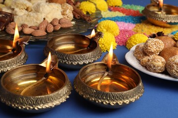 Obraz na płótnie Canvas Diwali celebration. Tasty Indian sweets, diya lamps and colorful rangoli on blue table, closeup
