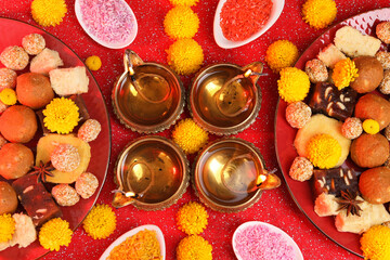 Diwali celebration. Flat lay composition with diya lamps and tasty Indian sweets on shiny red table