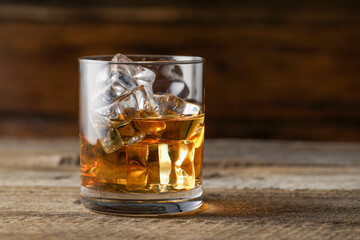 Whiskey with ice cubes in glass on wooden table, closeup. Space for text