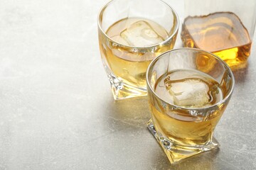 Tasty whiskey with ice in glasses on light table, closeup. Space for text
