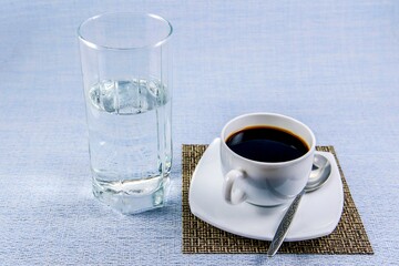 White cup of black coffee on a napkin-mat and a tall glass of mineral water on the table
