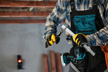 a worker in overalls and a protective helmet wearing yellow gloves cuts an iron hanger with...