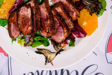 Fried duck breast in honey soy glaze with mixed salad and oranges.top veiw.