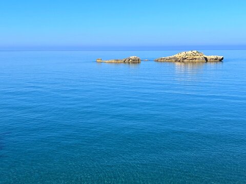 Blue sea calm water, rocks and clear sunny sky.