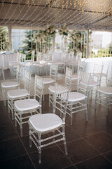 chiavari chairs. Outdoor wedding ceremony. wedding arch decorated with fresh white flowers with transparent chairs standing in the garden. Day of celebration, transparent chairs for guests