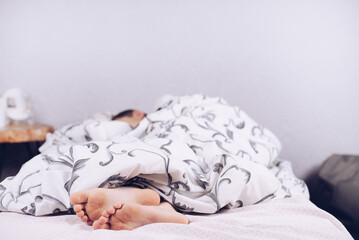 Bare feet of a child. The child is sleeping in bed. Legs look from under the blankets. Legs and heel