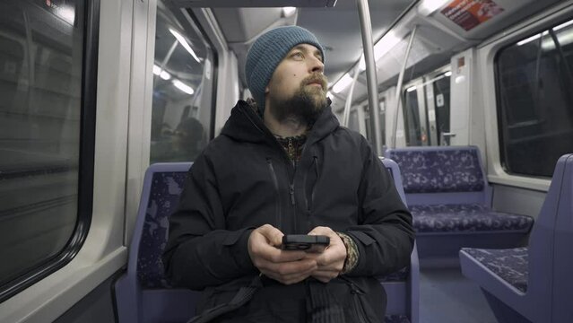 Man traveling on subway train in Hamburg sitting on blue seat and using smartphone wearing winter clothes. Hamburg metro commuter browsing internet on phone while commuting. Hamburger U-Bahn. 