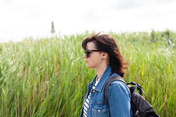 Young woman with backpack on a background of green grass and sky.
