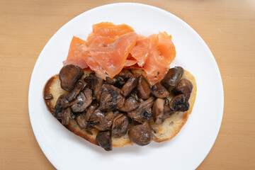 Fried mushrooms on sourdough toast with smoked salmon on a white plate seen from above. - 748246824