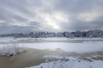 Rural winter landscape with a river covered in snow and footprints in the snow.