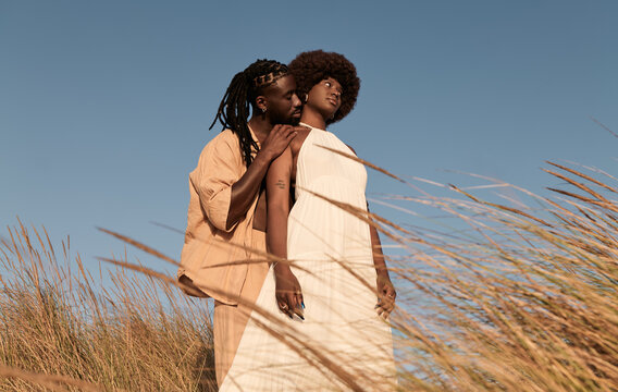 Happy black couple standing cuddling near dry grass plants in daylight