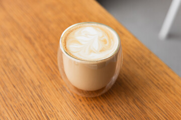 Glass of cappuccino coffee stands on wooden table, close-up photo