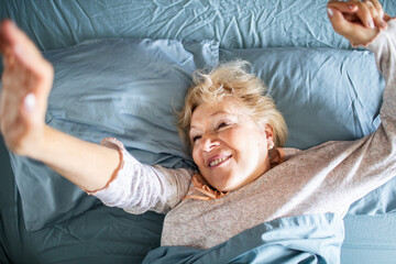 Smiling senior woman waking up in her bed at home