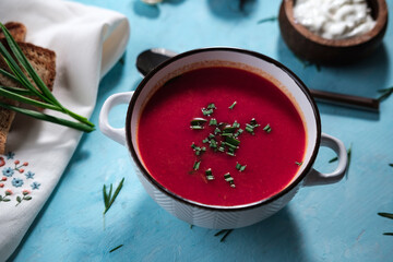 beetroot tomato soup with cream on blue wooden background, served with green herbs and tosted bread
