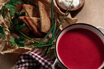 beetroot tomato soup with grilled bread, yoghurt or cream, wooden background served with table cloth textile and green garlic