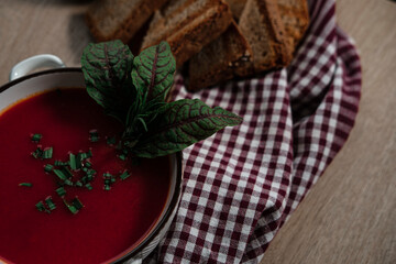 beetroot tomatoes soup in white bowl with handles served with crunchy triangle toasted bread, green beet leaves, green garlic, rustic cloth and wooden background