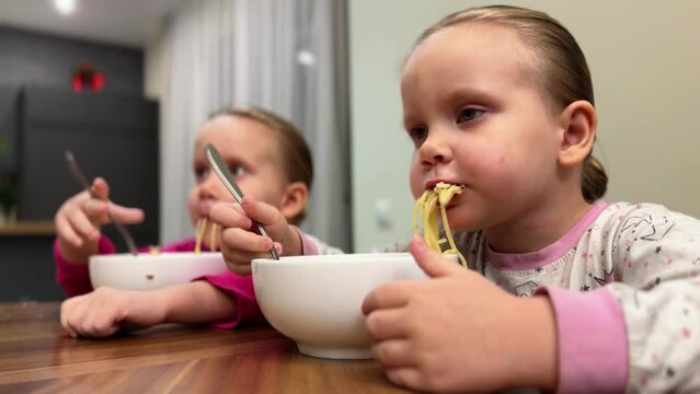 Twin kids in pajamas eating pasta from white plates