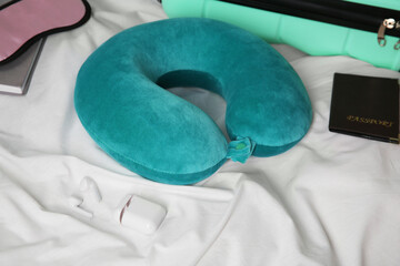 Turquoise travel pillow, suitcase, passport, sleep mask and earphones on bed
