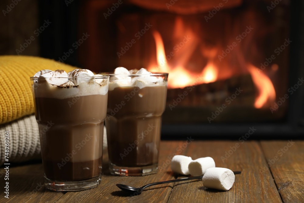 Sticker Glasses with hot cocoa, marshmallows and sweaters on wooden table near fireplace, space for text