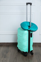 Turquoise travel pillow on suitcase near white wall indoors