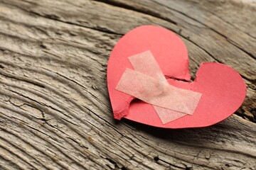 Broken heart. Torn red paper heart with medical adhesive bandages on wooden table, closeup with space for text