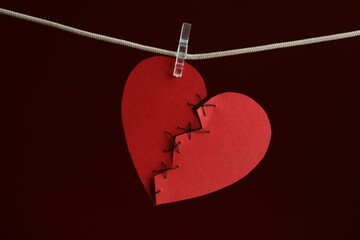 Broken heart. Torn red paper heart sewed with thread on rope against burgundy background