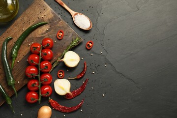 Cooking concept. Wooden cutting board and different products on black table, flat lay. Space for text
