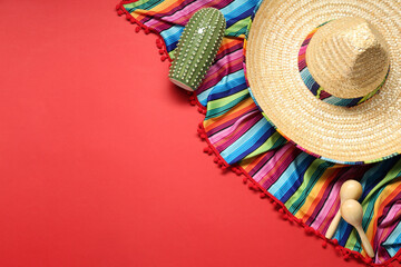 Mexican sombrero hat, toy cactus and colorful poncho on red background, flat lay. Space for text