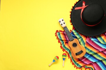 Mexican sombrero hat, guitar, maracas and colorful poncho on yellow background, flat lay. Space for...