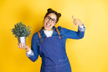 Young caucasian gardener woman holding a plant isolated on yellow background shouting with crazy...