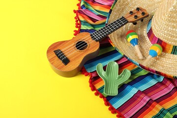 Composition with Mexican sombrero hat, ukulele and maracas on yellow table, closeup. Space for text