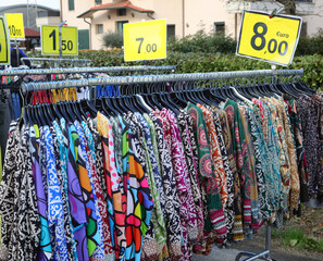 dresses  and colorful blouses made of cotton or polyester fabric hanging on hangers for sale in the...