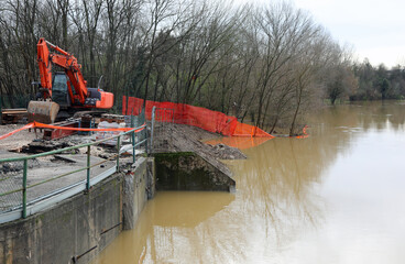 excavator on the embankment of the river during the flood in a road construction site to the...