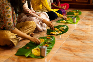 Traditional South Indian food served on plantain leaf on the floor and eaten by hand. Women wearing churidhars or kurtas - obrazy, fototapety, plakaty