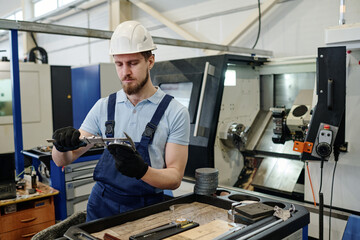 Young male turner working in modern factory measuring size of metal detail, copy space
