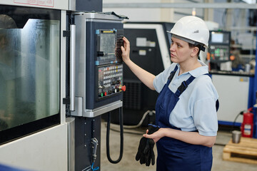 Modern female factory worker wearing uniform operating CNC machine, copy space
