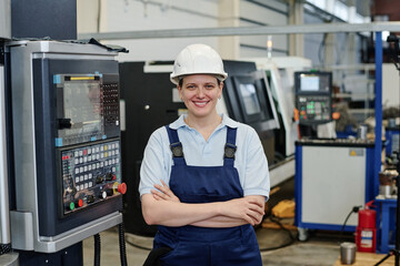 Medium portrait of self-confident female turner standing with arms crossed in factory workshop...