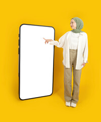 Touching huge display panel, full body view muslim woman wear hijab touching huge display panel. Using mobile application on big smartphone mock up. Advertising concept idea image, yellow background.