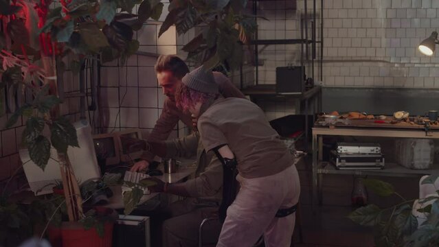 Young Black man monitoring security cameras on PC, calling friends and telling them to prepare for defense while having alarm signal with red light in post apocalypse bunkerYoung Black man monitoring 