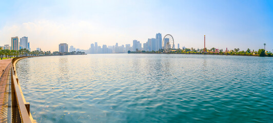 Panoramic skyline of downtown Sharjah and the Eye of the Emirates Ferris Wheel at Al Montazah Park island from the waterfront Corniche Central Souq Park Sharjah, United Arab Emirates.
